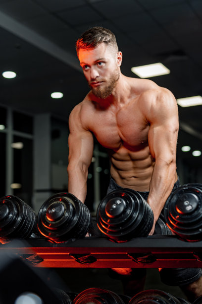 一个年轻的健康男子的肖像摆着金属哑铃。英俊的男人在努力训练前看着前方。图片下载