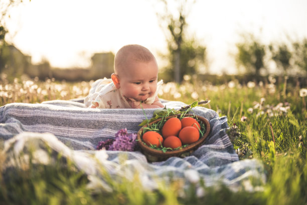 新生的女婴躺在草地上，看着篮子里放着复活节彩蛋图片下载