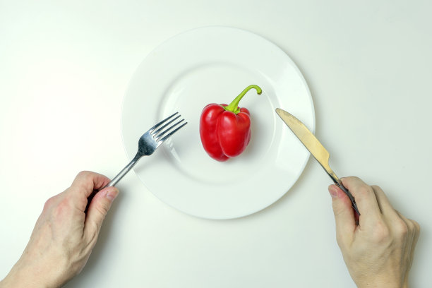 饮食的概念。男人的手拿着刀叉放在放着红辣椒的盘子上。图片下载