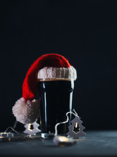 一杯圣诞烈性啤酒，戴着圣诞老人的帽子，背景是黑色的图片下载