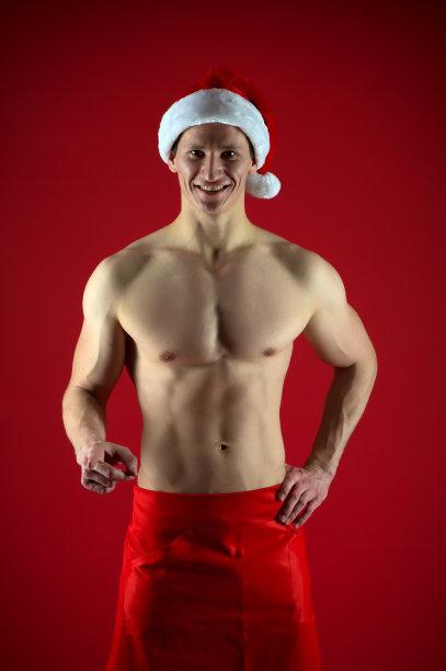 如果你是个坏女孩。男子性感肌肉躯干摆出自信的姿势。圣诞老人不仅会出现在好女孩身上。运动员戴圣诞老人帽，穿红色短裤。性感的运动男子在圣诞老人帽图片下载