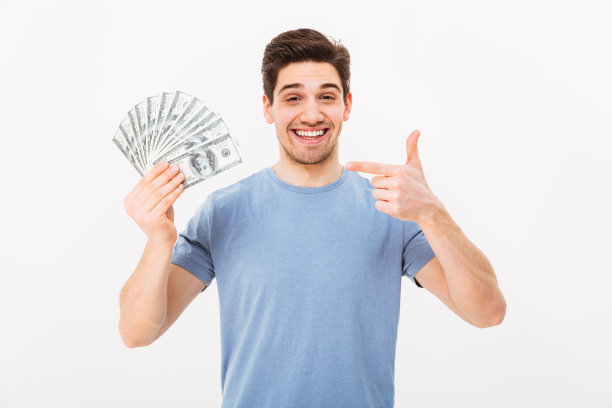 照片的快乐赢家的男人在休闲t恤微笑和指着扇子的钱在美元钞票，孤立的白墙图片下载