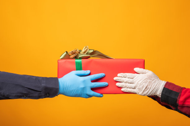 双手紧戴医用橡胶手套赠送礼物盒在圣诞节的黄色背景。圣诞快乐，恭贺新禧，送礼物。图片下载