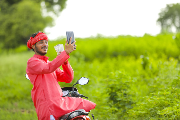 快乐的年轻印度农民坐在两轮车，在田地里自拍图片下载