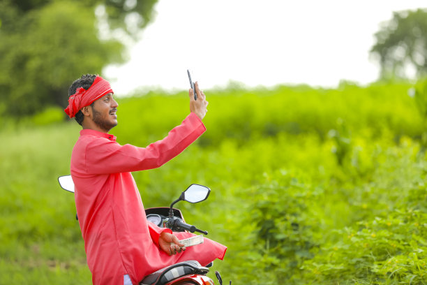 快乐的年轻印度农民坐在两轮车，在田地里自拍图片下载