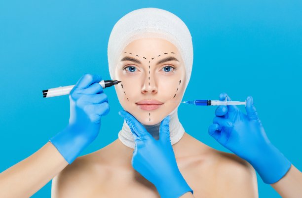 年轻女子的头部包裹着整形手术，周围是拿着注射器和皮肤标记的医生图片下载
