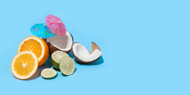 新鲜多汁的橙子，椰子和青柠与鸡尾酒伞孤立在蓝色的背景。健康饮食和节食的概念。旅游和假日概念。副本的空间。为你的文本留出空间图片下载