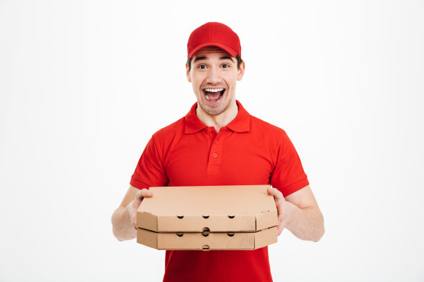 照片中，一名送餐员身穿红色t恤，头戴红色帽子，手里拿着两个外卖披萨盒，在白色背景下孤立无间图片下载