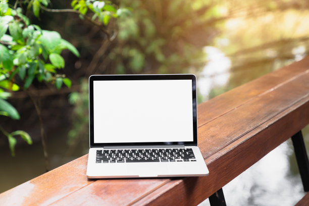 笔记本电脑的屏幕是空白的放置在一个木桌和树木与自然，是一个美丽的小雨天。图片下载