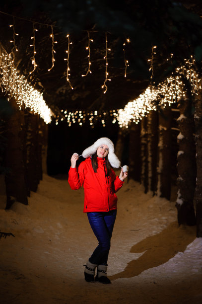 户外照片年轻美丽的快乐微笑的女孩，摆姿势在装饰着灯泡的小巷。圣诞集市的背景。图片下载