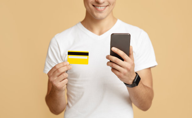 身着白色t恤的快乐千禧一代男士看了看智能手机，拿着信用卡付款图片下载