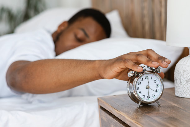 困倦的黑人躺在床上关掉闹钟图片下载