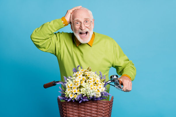 退休老人的照片骑自行车野花盒子张开嘴手头戴眼镜绿色套头孤立的蓝色背景图片下载