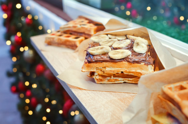 在圣诞和新年的灯光背景下，在圣诞市场街头小吃咖啡馆里的比利时华夫饼配上香蕉和巧克力酱图片下载
