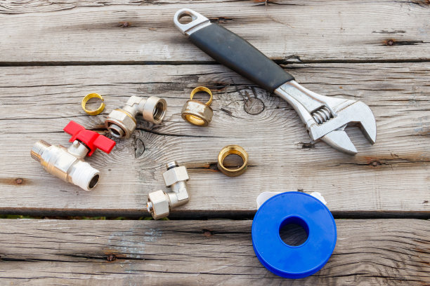 各种管道配件，密封胶带和可调扳手在乡村木制背景。俯视图图片下载