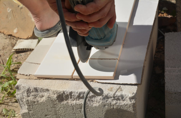 一个建筑承包商正在使用电动角盘磨床切割陶瓷墙砖。图片下载