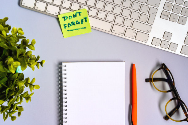 键盘上贴着一张写着“不要忘记”的贴纸。从上面的桌面照片与办公用品和一个空记事本。空间的文本图片下载