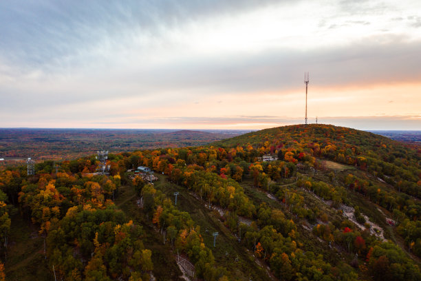美丽的无人机照片肋山与彩色的秋天树叶或秋天的树叶衬里的草地滑雪在日落时，多云的天空变成橙色和粉红色的地平线上跑。图片下载