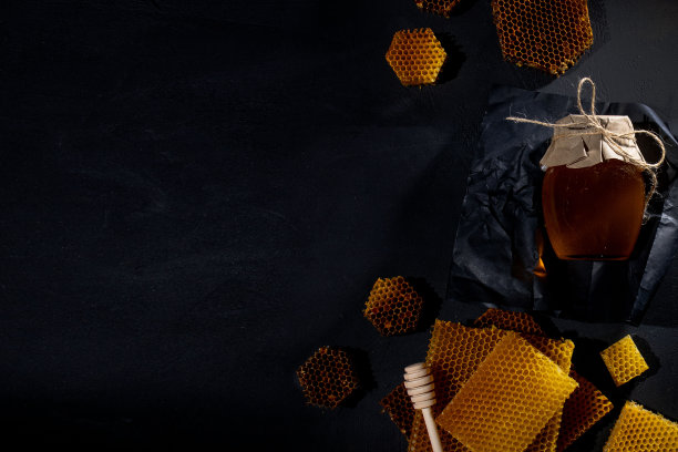 蜂蜜在一个罐子和一个蜂巢。在黑色的木制背景上。文本的空闲空间。前视图。图片下载