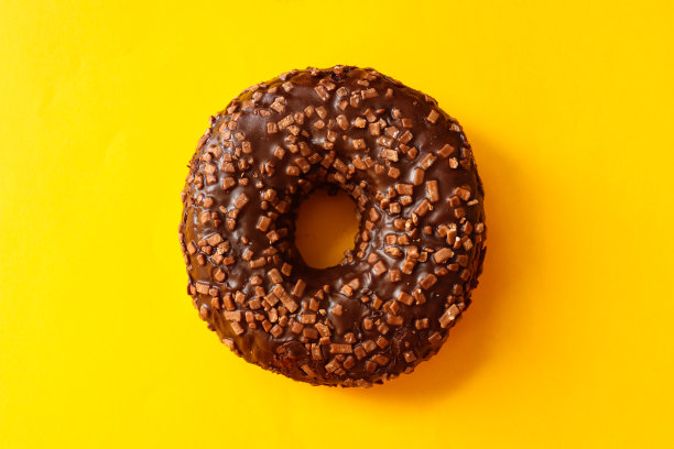 在明亮的黄色背景上近距离地点缀着巧克力光泽的甜甜圈。平躺，俯视图图片下载