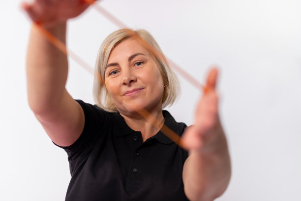 一个女人的肖像拉伸一个健康的橡皮筋与她的手和摆姿势。白色背景上的照片。年龄和健康生活方式概念，流行病。图片下载