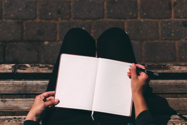 女性手里拿着空白的笔记本一起拿着笔，坐在公园的长椅上，俯视图。女人的手拿着笔记本。把你所有的梦想都写在笔记本上。用钢笔书写。空间的文本图片下载