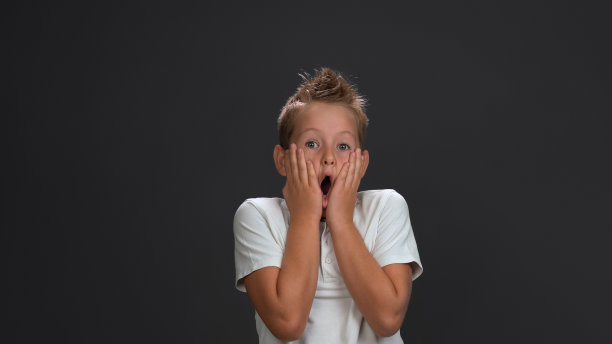 十几岁的男孩表达了omg或震惊的情绪，张开嘴，把手掌放在脸颊上。销售的概念。孤立在灰色背景。本空间图片下载