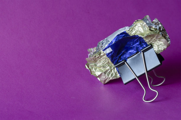 粉碎的糖果包装纸和金属黑色夹在紫色的背景。图片下载