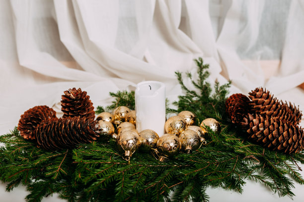 斯堪的纳维亚圣诞贺卡与白色织物和圣诞花环与白色蜡烛内。绿色的冷杉枝，松果，金色的球和蜡烛在白色的背景与文字的空间。图片下载