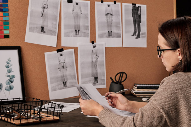 年轻的当代时装设计师与照片在工作室的桌子图片下载