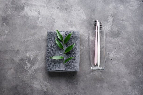 将牙刷放在玻璃杯里，用毛巾在灰色的背景上铺成平铺状。图片下载