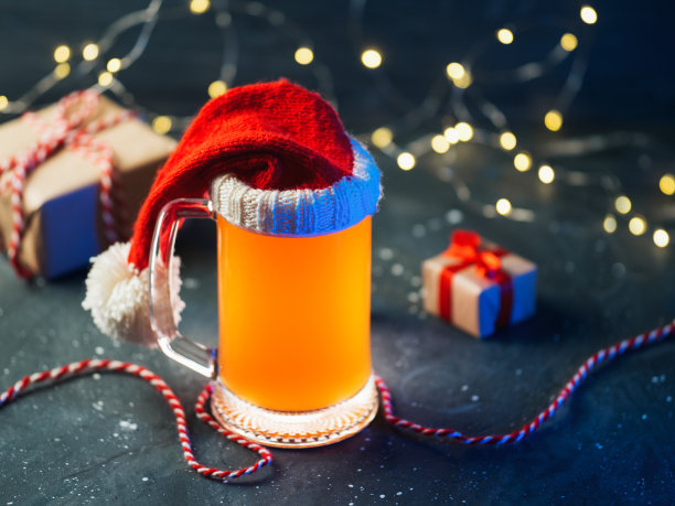 桌上放着一大杯圣诞啤酒，戴着圣诞帽，还有礼盒和花环图片下载