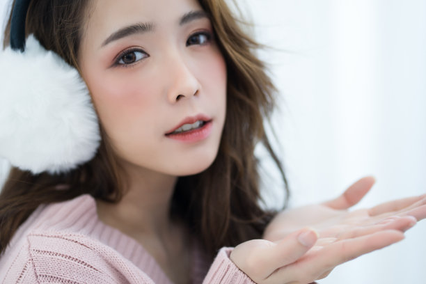 美丽的亚洲女孩寒冷穿着白色耳套和温暖的毛衣粉色寒冷在家，概念女人的生活方式和冬天。图片下载