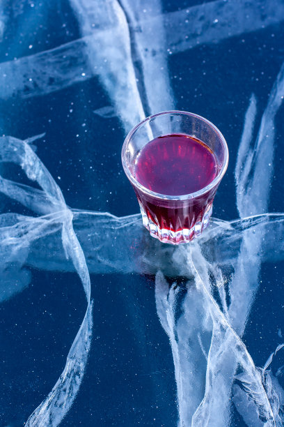 湖面上放着一只盛着红色药水的玻璃杯。杯中的酒精和有漂亮的深裂缝的冰。垂直的。图片下载