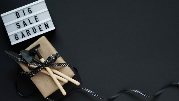 横幅概念黑色星期五庆祝，字母。白色板与文字大销售花园，礼品盒与黑豌豆弓和花园工具在黑色背景，俯视图，平面lay，复制空间。图片下载