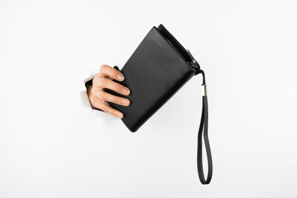 一个女人的手从墙上的一个洞里掏出了一个黑色的钱包。图片下载