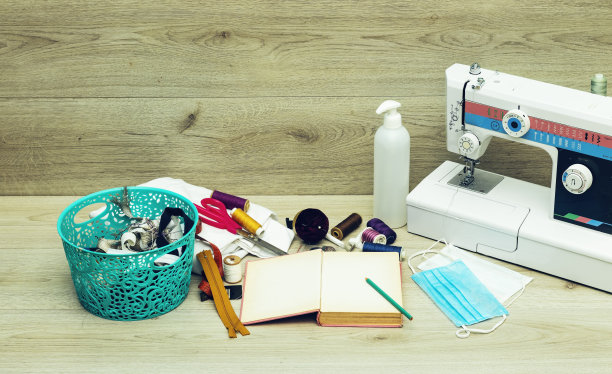 设计师工作地点缝纫机和医用口罩，胶岛和缝纫工具篮子:剪刀，彩色线轴和压脚在灰色的木制桌子上图片下载