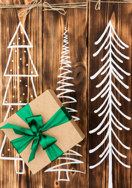 礼物在牛皮纸与绿色丝带在一个乡村烧焦的木头背景与彩绘的圣诞树。前视图。图片下载