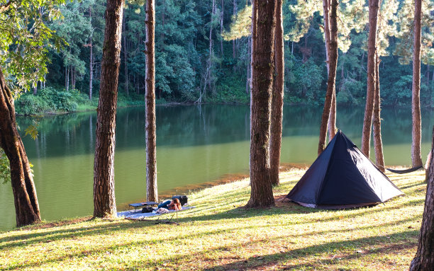 一个女人躺在一个帐篷旁边的垫子上，在湖边的公园里享受露营图片下载