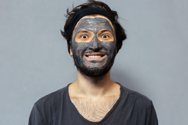 肖像的年轻微笑披头散发的家伙与面具的背景灰色的背景。图片下载