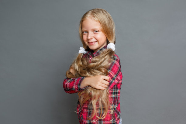 扎着马尾辫的小女孩孤立地站在灰色的怀抱里，看起来很开心图片下载