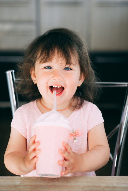 一个穿着粉红色裙子的小女孩坐在厨房里用粉红色的鸡尾酒杯喝着酒图片下载