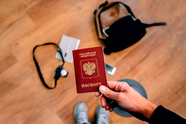 一名男子持有俄罗斯护照，背景中有背包和旅行用品。旅行的概念。从上面的照片。图片下载