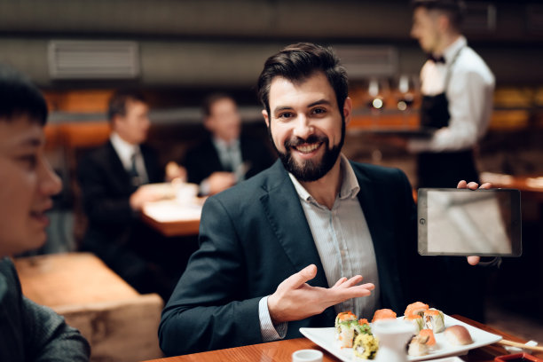 在饭店会见中国商人。男人正在展示平板电脑。图片下载