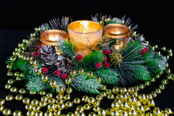 圣诞装饰在黑色背景下的烛光。由金球和珠子组成，带有图案的镂空烛台和圣诞树的树枝。优雅的蛋卷和红色的浆果图片下载