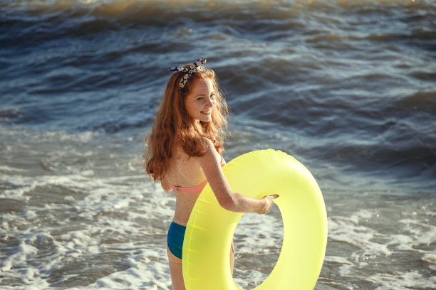 年轻美丽的女人是放松在日落的海滩与橡胶圈。图片下载