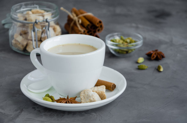 奶茶，肉桂，豆蔻，茴香和其他香料，印度马沙拉茶在白色的杯子在黑暗的背景。副本的空间。图片下载