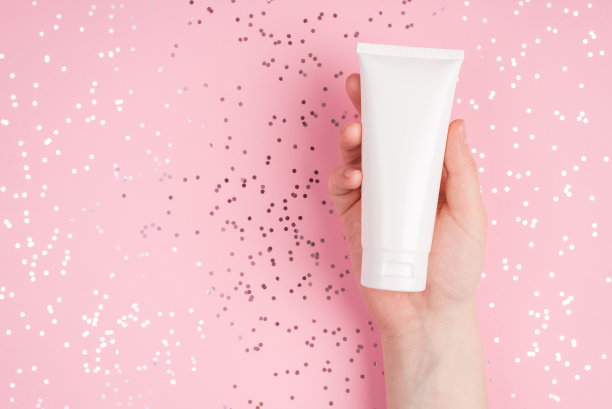 护肤理念。靠近顶部上方的俯视图照片的女性手显示奶油瓶在淡粉色的桌子背景与闪亮的点图片下载