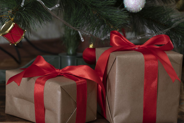 两件用牛皮纸包着的礼物和一条红色的宽丝带放在一张黑色背景的木桌上。图片下载