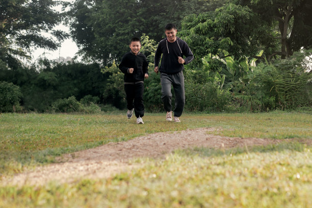 亚洲十多岁的男孩和年轻的父亲一起慢跑在自然小径绿色森林公园与轻微的晨雾。健康的生活方式的概念。图片下载